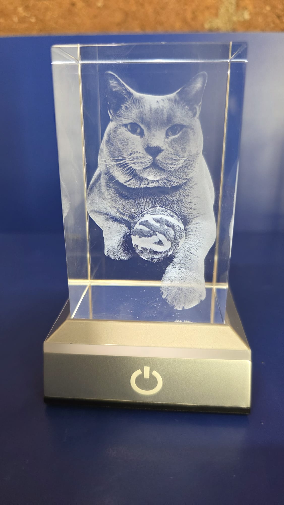 Figura de cristal grabada con láser en 3D que muestra el retrato realista de un gato junto a un ovillo de lana on base luminosa