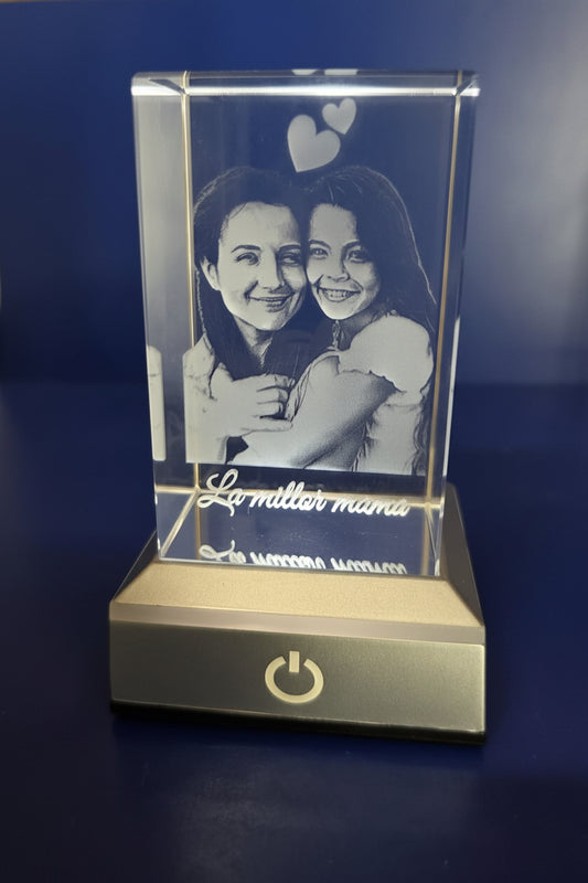 Cubo de cristal iluminado con el grabado 2D de dos personas abrazándose, corazones y la dedicatoria La millor mama